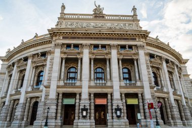 Avusturya 'nın Viyana kentindeki Burgtiyatronun ön manzarasında, Neo-Rönesans mimarisi, büyük sütunlar, parlak gökyüzü altında heykel ayrıntıları, zarafet, kültür ve tarihi Avrupa tiyatro mirası sergileniyor..