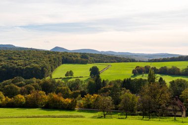 Ormanlık tepeleri, açık çayırları ve yumuşak bir gökyüzünün altındaki uzak dağları olan yuvarlanan yeşil kırsal bölge. Seyahat veya yaşam tarzı kullanımı için doğa, tazelik ve açık hava sükunetini aktaran huzurlu kırsal alan.