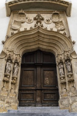 Gotik kilise girişini oyma taş kemer, ahşap çift kapı, dini heykeller ve kapının üstündeki dekoratif arma ile süsleyin..