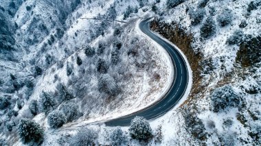 aerial view from above of a road through forest in winter.