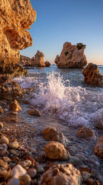 Sahilde gün batımında, arka planda Kiril adasının kıyılarında kayalar ve dalgalar vardı.
