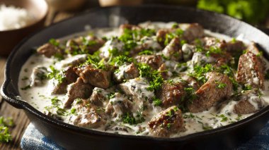 Ekşi kremalı biftek ve domuz ciğeri. Tahta bir masada demir kızartma tavası.