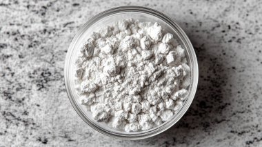 Gri dokulu bir masada beyaz bir kasede beyaz şeker yığını.