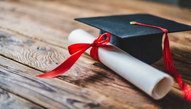 kırmızı mezuniyet şapkası ve diploması ahşap masada..