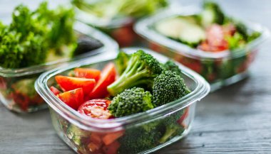 Tahta masanın üzerinde farklı yeşil sebzeler olan plastik bir kutu.