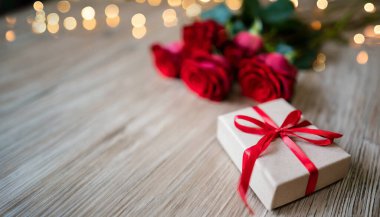 Kırmızı fiyonklu hediye kutusu ve ahşap arka planda güller