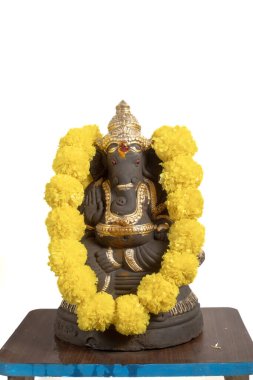 Altın süslemeli koyu gri Ganesha heykeli, parlak sarı kadife çiçekli bir çelenkle kaplıydı. Hindu ayinlerine, sunaklara ve kültürel dekorasyonlara uygun..