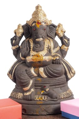 Altın aksanlı dekoratif Ganesha putu beyaz arka planda bir hediye kutusunun yanına yerleştirilmiş. Festival promosyonları, ruhani temalar, dini kutlamalar, ürün sergileri ve Hint kültürel görselleri için ideal..