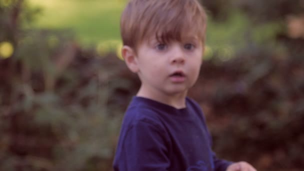 Il piccolo ragazzo biondo si gira verso la telecamera al rallentatore fuori nell'area verde . — Video Stock