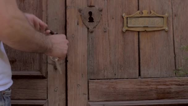 L'homme déverrouille la vieille porte en bois avec des clés et entre dans la maison en mo lent — Video