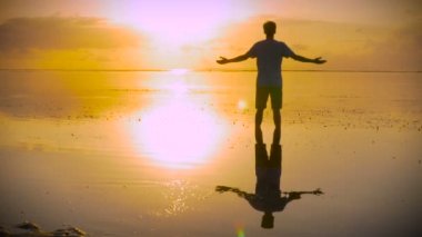 İbadet eden adam sahilde poz vererek güneşe doğru uzanıyor Şükürler