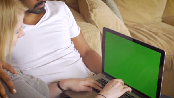Two people sit on a sofa with a green screen laptop and surf the internet — Stock Video