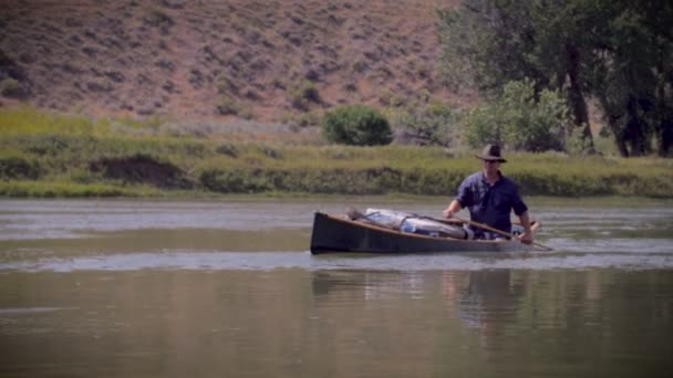 Middle age outdoorsman paddles a blue canoe down a river — Stock Video