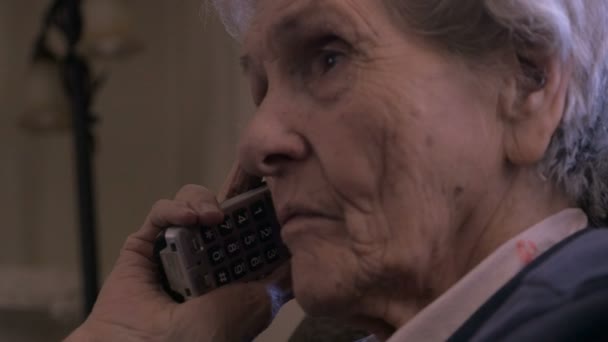 Una mujer de 90 años escucha con atención en un teléfono inalámbrico en un cuarto oscuro — Vídeos de Stock