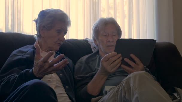 Zwei Senioren sitzen nebeneinander und unterhalten sich mit einem mobilen Tablet-Dolly — Stockvideo