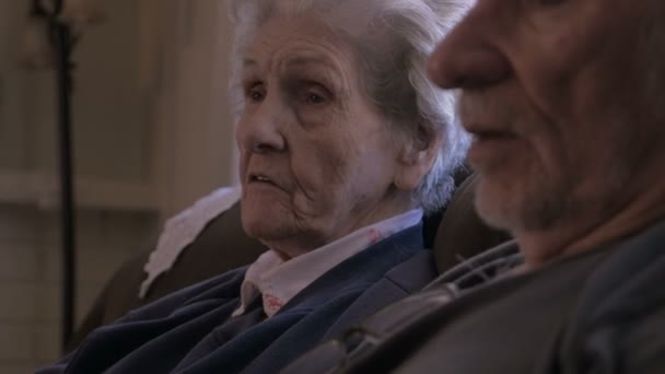 Два пожилых человека разговаривают, сидя рядом друг с другом на диване — стоковое видео