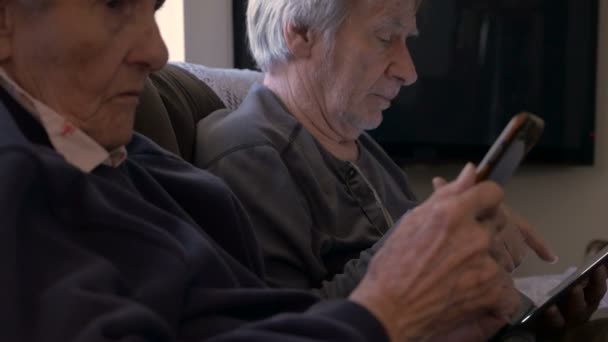 90-åriga kvinnor och sonen ser på sina mobila enheter, en mobiltelefon och tablet — Stockvideo