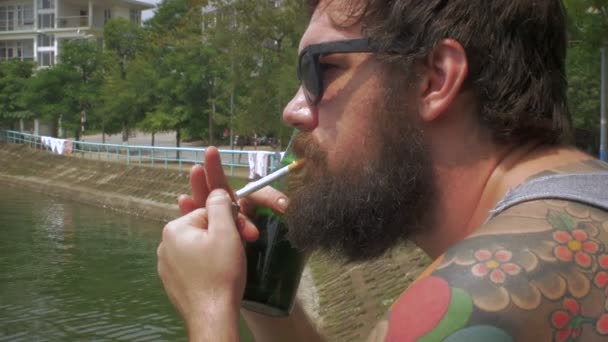 Portrait of a bearded man lighting a cigarette and smoking outside by a lake — Stock Video