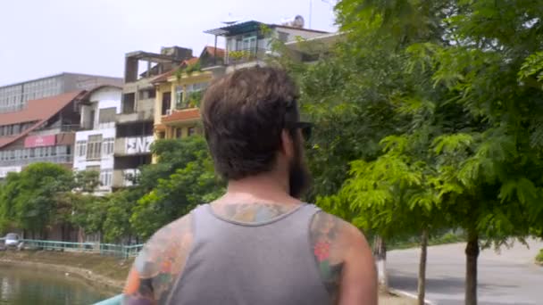 Steadicam follows a bearded young man with tattoos waiving to people — Stock Video