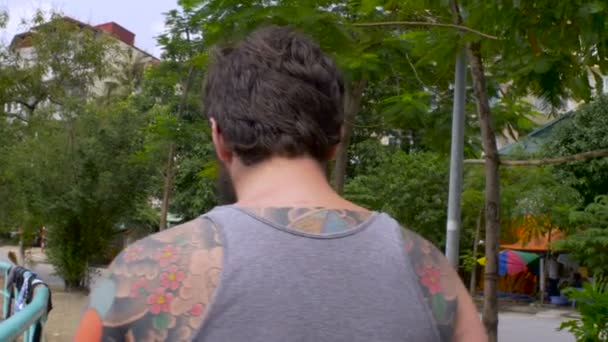 Bebaarde man met volledige rug tattoo en zonnebril loopt weg van de camera — Stockvideo