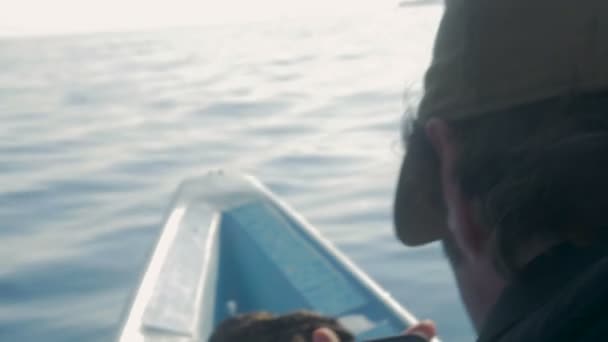 En man kontrollerar sin telefon när du sitter på framsidan av en liten båt — Stockvideo