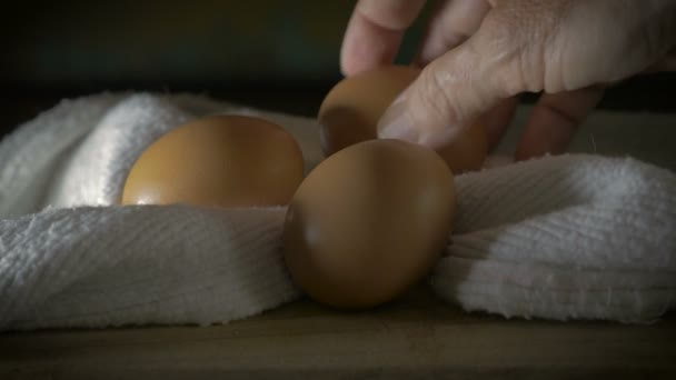 A hand picks up brown eggs from a wooden cutting board with a cotton cloth — Stock Video