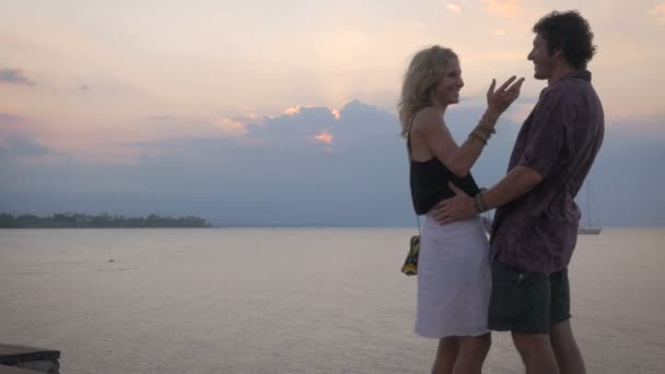 Een aantrekkelijke paar kussen en omhelzen met uitzicht op de Oceaan bij zonsondergang in het paradijs — Stockvideo