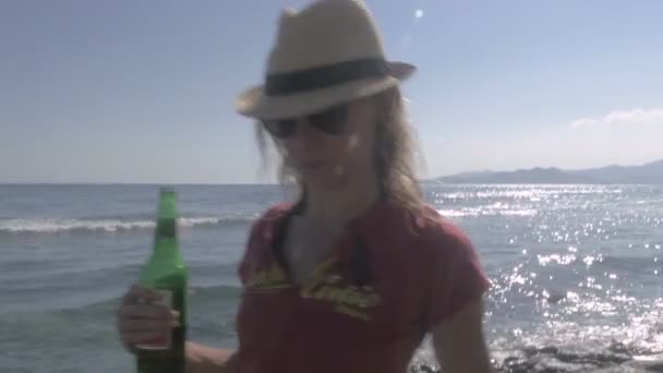 Yakışıklı bir genç kadın bir bira ile sahilde yürüyor — Stok video