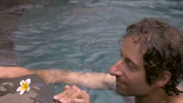 Middle aged man swims up to a glass of white wine in a pool and takes a drink — Stock Video