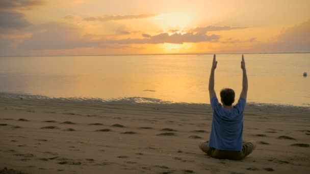 Un hombre sentado en una pose de loto yoga en brazos que bajan del océano y se extiende — Vídeos de Stock