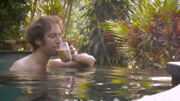 Un hombre de mediana edad bebe una taza de café en una piscina infinita en un hotel de lujo — Vídeo de stock