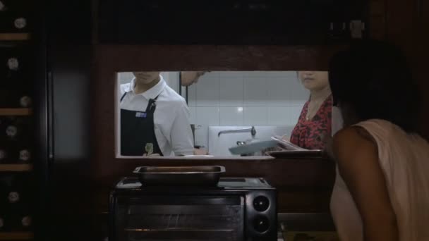 Zusammenarbeit in einem belebten Restaurant mit Blick durch ein Fenster zur Küche — Stockvideo