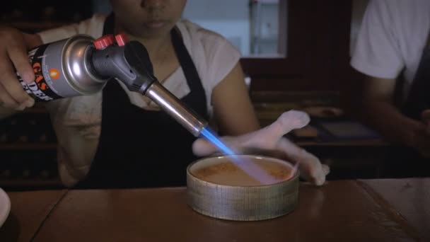 Ein Koch verwendet eine Taschenlampe, um die Oberseite der Creme Brule zu karamellisieren — Stockvideo