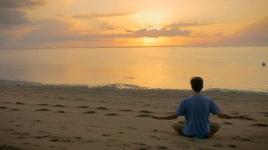 Bir lotus poz gündoğumu sırasında okyanusa bakan bir adam oturuyor