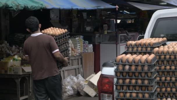 A man carries crates of eggs from the back of his pickup truck into a market — Stock Video
