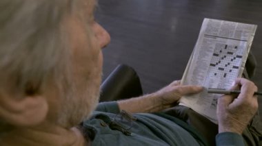 Yaşlı bir kıdemli bir bulmaca bir gazetede Ots ile bir sandalyede oturur