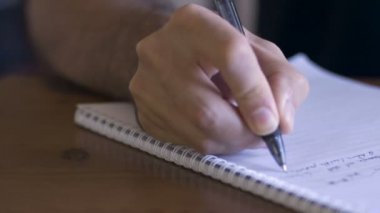Bir adam bir sarmal bağlı kağıt defterde yazıyor bir kalemle - dolly yakın çekim