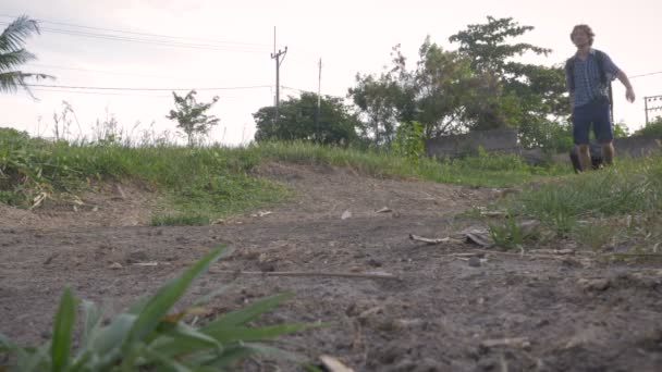 Disparo de ángulo bajo de un hombre caminando por un camino de tierra con su equipaje — Vídeo de stock