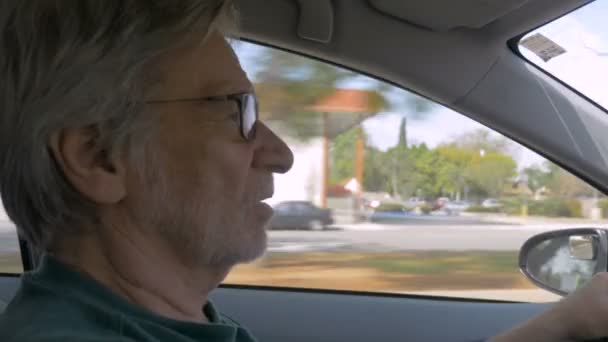 Hand held of an elderly senior man driving a car during the day and talking — Stock Video