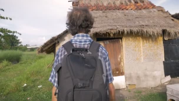 Un turista se acerca a una casa abandonada y llama a la puerta con un disparo en la mano — Vídeo de stock