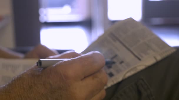 Hand gehouden close up van een senior hand werken een kruiswoordpuzzel in de krant — Stockvideo