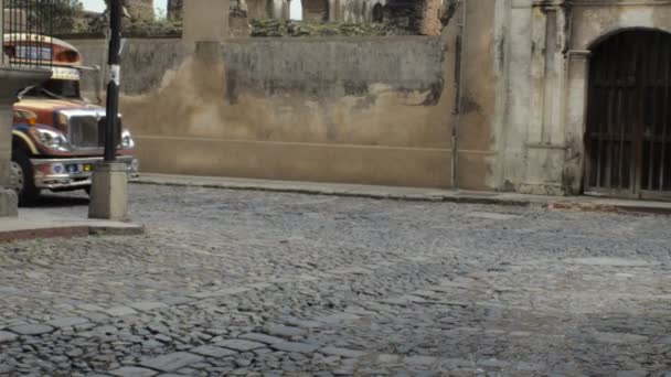 Un vecchio scuolabus addobbato passa davanti alle rovine di una chiesa di Antigua — Video Stock