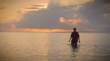 Okyanustan gelen ışık ışınları ile bir gün batımı sırasında insan yürüyor