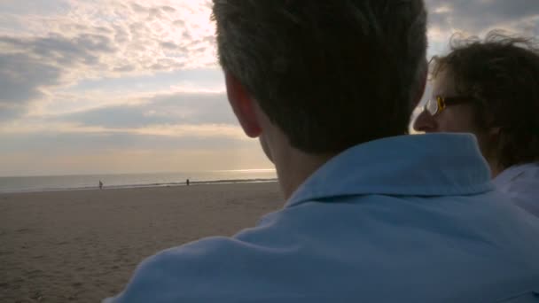 Рука тримала стрілянину двох чоловіків, які розмовляли і спостерігали за заходом сонця над океаном — стокове відео