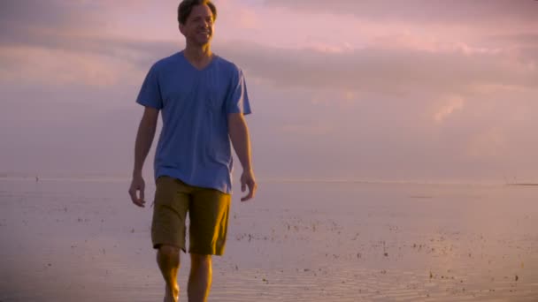 한 중 년 남자와 해돋이 또는 일몰에 카메라 쪽으로 해변에 산책 — 비디오