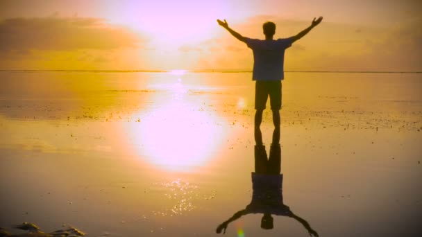 Man moves into lotus pose on beach reaching out towards the sun — Stock Video