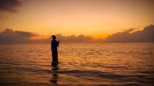 Siluett av Man dyrkar med huvudet upp till himlen och händer i bön i havet — Stockvideo