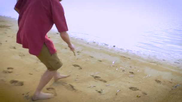 A man runs up to the waters edge and draws a dollar sign in the sand — Stock Video