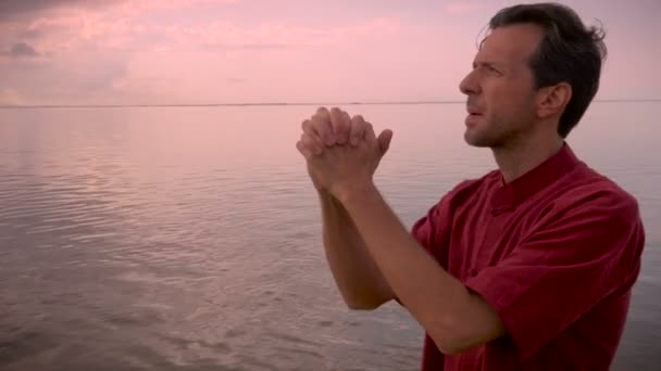 Χέρι-κρατημένα πυροβολισμό ενός άνδρα που κλείνει τα μάτια του σε προσευχή που στέκεται στο νερό — Αρχείο Βίντεο