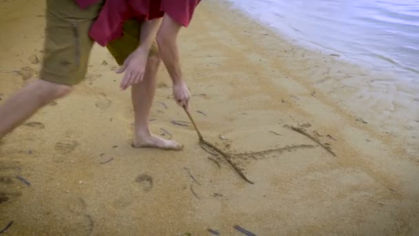 Hombre atractivo escribe Te amo en la arena en la playa con un palo — Vídeos de Stock